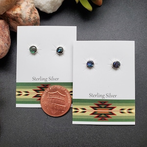 May include: Two pairs of sterling silver earrings with abalone shell inlays. The earrings are displayed on white cards with the text "Sterling Silver". A penny is included for size reference.