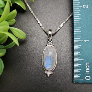 May include: A silver chain necklace with a silver oval pendant featuring a blue and white moonstone. The pendant is approximately 1 inch long.
