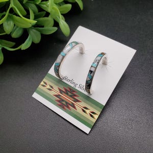 May include: A pair of sterling silver hoop earrings with turquoise and white stone inlay. The earrings are displayed on a card with the text "Sterling Silver".