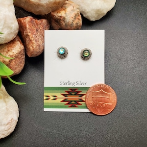 Puede incluir: Un par de pendientes de plata de ley con piedras iridiscentes azules y verdes. Los pendientes se muestran en una tarjeta blanca con las palabras "Sterling Silver" impresas en ella. Un centavo de dólar estadounidense se incluye como referencia de tamaño.