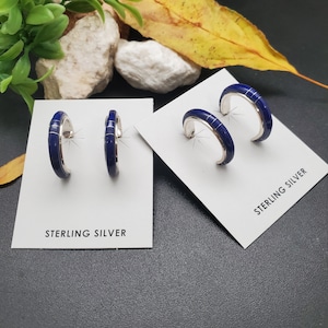 Peut inclure: Deux paires de boucles d'oreilles créoles en argent sterling avec incrustations bleues. Les boucles d'oreilles sont présentées sur des cartes blanches avec le texte "STERLING SILVER".