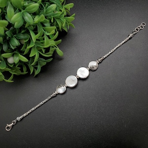 May include: A silver bracelet with four white mother-of-pearl round beads and intricate silver detailing.