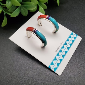 May include: A pair of sterling silver hoop earrings with inlaid turquoise, red, and purple stones. The earrings are displayed on a white card with a turquoise geometric border. The card has the text "Sterling Silver".