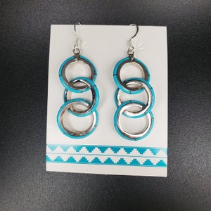 May include: A pair of silver earrings with turquoise accents. The earrings are made of three interlocking circles.