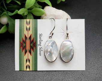 May include: Sterling silver earrings with oval shaped white mother of pearl stones. The earrings are on a white card with the words "Sterling Silver" printed on it.