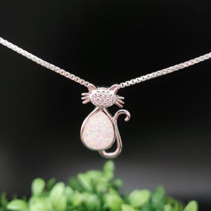 May include: A silver necklace with a white opal cat pendant. The cat has a silver outline and is set with small clear stones.