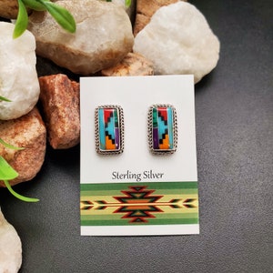 May include: Sterling silver earrings with a rectangular inlay of turquoise, red, orange, green, purple, and black stones. The earrings are displayed on a white card with the text "Sterling Silver" and a Southwestern-style design.