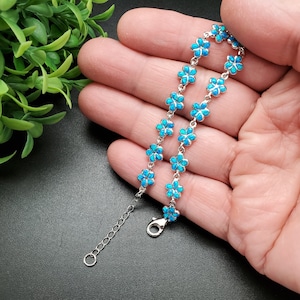 May include: A silver bracelet with a delicate chain and blue opal flower charms. The bracelet has a lobster clasp closure.