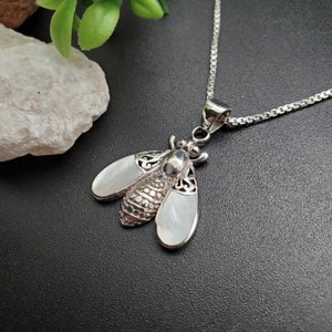 May include: A silver necklace with a white mother of pearl bee pendant. The bee has intricate details and is a delicate piece of jewelry.