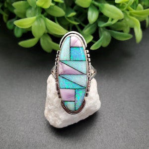 Pode incluir: Um anel de prata com uma pedra ovalada engastada em um padrão geométrico de turquesa, rosa e opala branca.