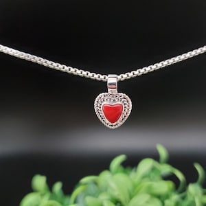 May include: A silver chain necklace with a small heart pendant. The heart is red and has a silver border.