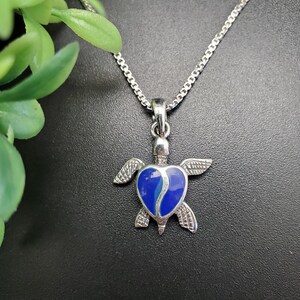 Può includere: Collana con pendente a forma di tartaruga color argento con guscio blu e argento a forma di cuore. La tartaruga ha ali dettagliate e una catena delicata. Il pendente è lungo circa 2,5 cm.