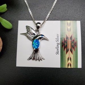 May include: Sterling silver hummingbird pendant necklace with a blue opal gemstone. The hummingbird is in flight with its wings spread out.