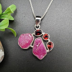 Peut inclure: Un collier en argent avec un pendentif composé d'un groupe de pierres précieuses roses et rouges. Le pendentif est composé de plusieurs pierres de forme irrégulière, dont certaines sont facettées. Le collier est de style chaîne délicate.