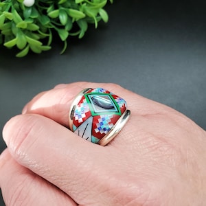Puede incluir: Un anillo ancho de plata con un patrón geométrico rojo, verde, azul y blanco incrustado con turquesa y concha de abulón.