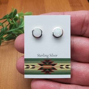 May include: A pair of sterling silver earrings with white opal stones. The earrings are displayed on a white card with the text "Sterling Silver" and a southwestern design.