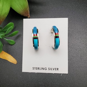 May include: Sterling silver hoop earrings with turquoise and multi-colored inlay. The earrings are displayed on a white card with the text "STERLING SILVER".
