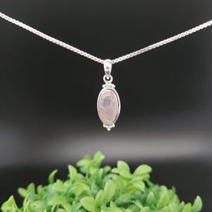 May include: A silver chain necklace with a pendant featuring a light pink oval gemstone.