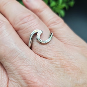 May include: A silver wave ring with white opal inlay. The ring is on a person's finger.