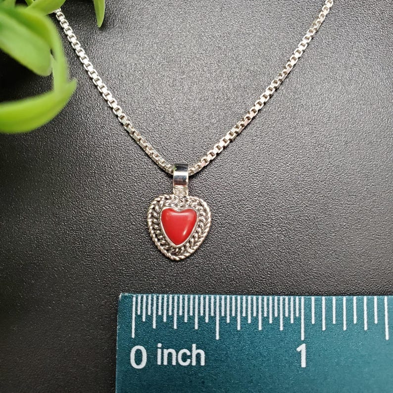 May include: A silver chain necklace with a red heart pendant. The pendant is about 1 inch in diameter and has a detailed design.
