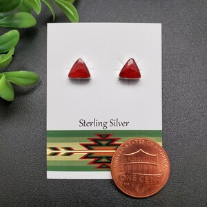May include: A pair of sterling silver earrings with red triangular stones. The earrings are displayed on a white card with the words "Sterling Silver" printed on it. A penny is included for size reference.