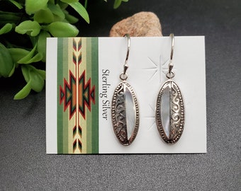May include: Sterling silver earrings with a white oval mother of pearl inlay and a filigree design. The earrings are on a white card with the words "Sterling Silver" printed on it.
