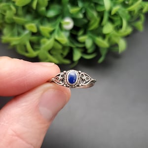 Könnte beinhalten: Ein silberner Ring mit einem blauen ovalen Edelstein, der in einem filigranen Design gefasst ist.