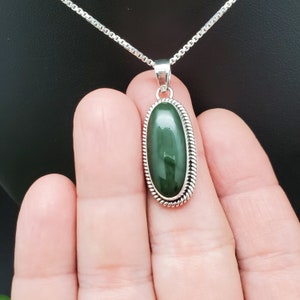 K&ouml;nnte beinhalten: Eine silberne Kettenkette mit einem ovalen Anh&auml;nger aus gr&uuml;nem Jade. Der Anh&auml;nger ist in einer silbernen Fassung mit einem seilartigen Rand gefasst.