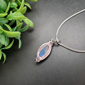 May include: A silver necklace with a pendant featuring a blue and green iridescent gemstone set in a silver oval frame.