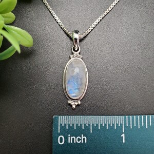 May include: A silver chain necklace with a silver oval pendant featuring a blue and white moonstone. The pendant is approximately 1 inch long.