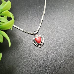May include: A silver chain necklace with a heart-shaped pendant featuring a red coral stone.