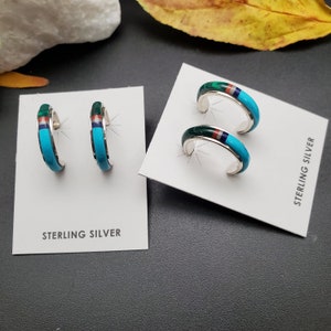 May include: Two pairs of sterling silver hoop earrings with turquoise, red, and green inlay. The earrings are displayed on white cards with the text "Sterling Silver".