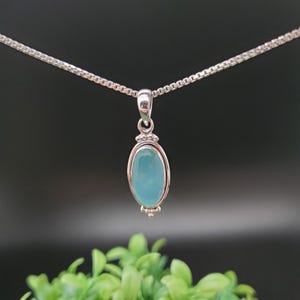 May include: A silver chain necklace with a pendant featuring a light blue oval gemstone set in a silver bezel.