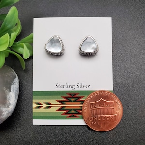 May include: A pair of sterling silver earrings with a triangular shaped white mother of pearl stone. The earrings are displayed on a white card with the words "Sterling Silver" printed on it. A penny is included for size reference.