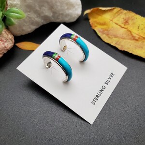 May include: A pair of sterling silver hoop earrings with turquoise, red, and blue inlay. The earrings are displayed on a white card with the text "STERLING SILVER".