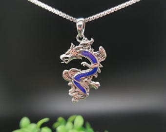 May include: A silver dragon pendant necklace with blue enamel detailing. The dragon is curled in a defensive position with its wings spread.