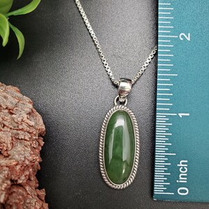 K&ouml;nnte beinhalten: Eine silberne Kettenkette mit einem gr&uuml;nen ovalen Anh&auml;nger. Der Anh&auml;nger ist in einen silbernen Rahmen mit einem Seil-Design gefasst. Der Anh&auml;nger ist etwa 2,5 cm lang.