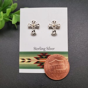 May include: Sterling silver cross earrings with a black and white design and a gold accent. The earrings are displayed on a white card with the words "Sterling Silver" printed on it. A penny is included for size reference.
