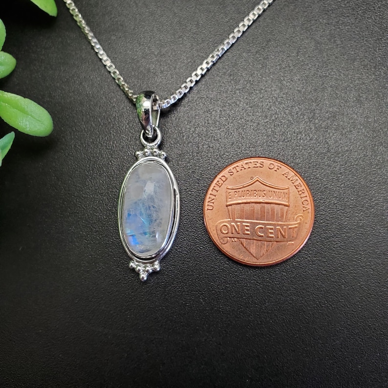 May include: A silver chain necklace with a silver oval pendant featuring a moonstone. The pendant is about the size of a US penny.