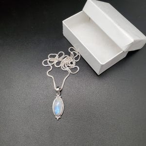 May include: A silver chain necklace with a silver oval pendant featuring a blue moonstone.