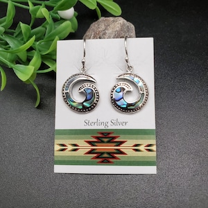 May include: A pair of sterling silver earrings with a swirl design featuring abalone shell inlay. The earrings are displayed on a white card with the text "Sterling Silver" printed on it.