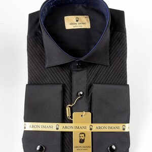 May include: A black dress shirt with a pleated front and French cuffs. The shirt has a gold label with the text "ARON IMANI" and a small beard icon. The shirt is made in Turkey.