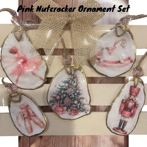 May include: Set of five pink and gold Christmas ornaments featuring a ballerina, a rocking horse, a Christmas tree, a pair of ballet shoes, and a nutcracker. The ornaments are made of paper mache and have a rustic, vintage look.
