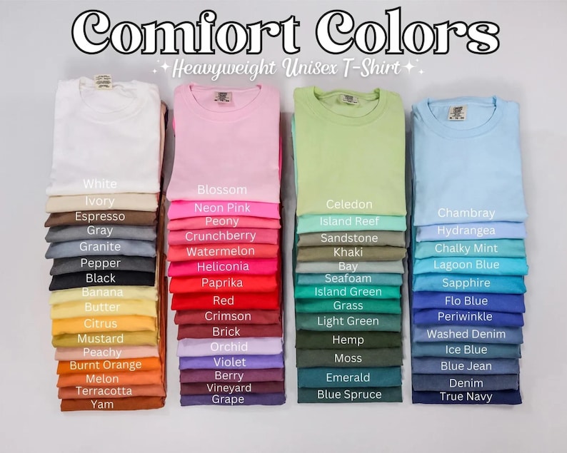 May include: Stacks of folded Comfort Colors heavyweight unisex t-shirts in various colors, including white, pink, green, and blue. Each stack is labeled with the color name, such as "Blossom," "Chambray," and "Black."