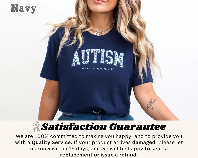 May include: Navy blue t-shirt with the word "AUTISM" in white, floral-patterned letters. The word "awareness" is written below in a script font. The shirt is a crew neck and has short sleeves.