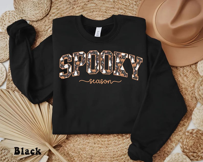 Black sweatshirt with spooky season design featuring ghosts, pumpkins, and flowers, ideal for fall outfits or Halloween gift.