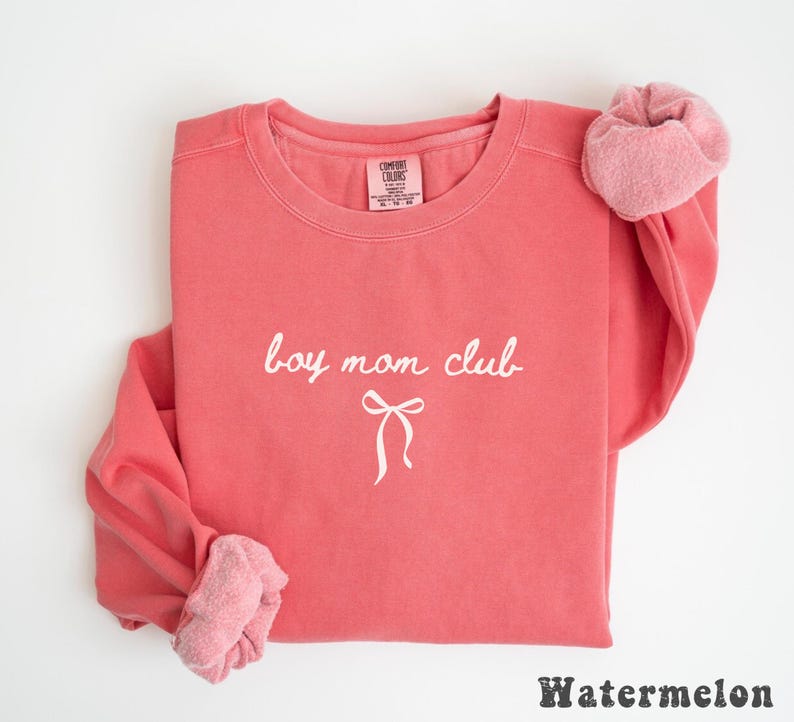 K&ouml;nnte beinhalten: Ein korallenfarbenes Sweatshirt mit dem wei&szlig;en Schriftzug "boy mom club" und einer Schleifen-Grafik. Das lang&auml;rmlige Oberteil hat einen Rundhalsausschnitt. Unten steht das Wort "Watermelon".