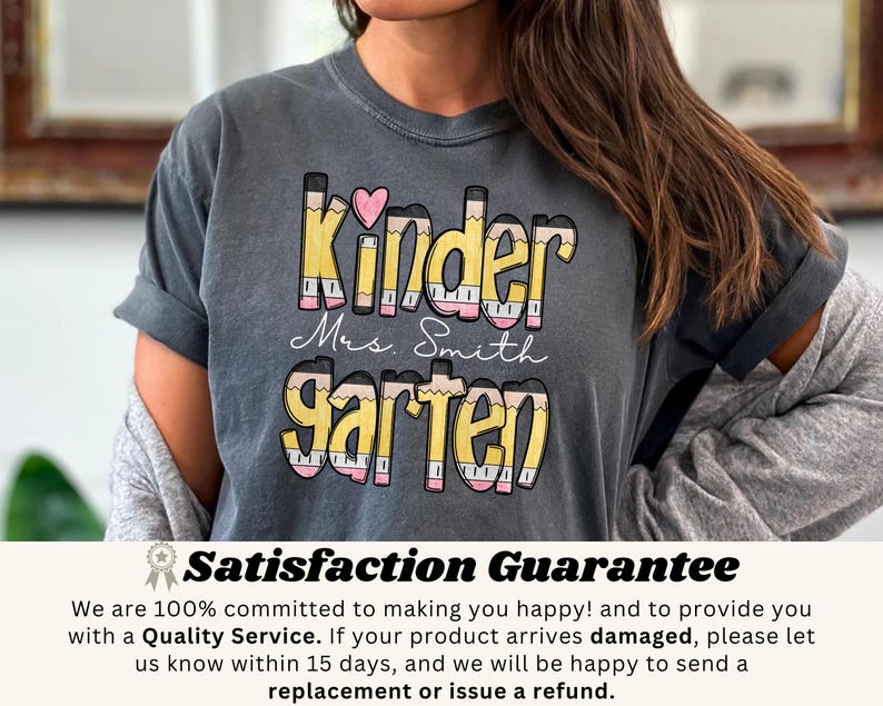 May include: A gray t-shirt with the words "Kinder Mrs. Smith Garten" in a colorful pencil-themed design. The word "Kinder" has a pink heart above it. The shirt is a comfortable, casual style.