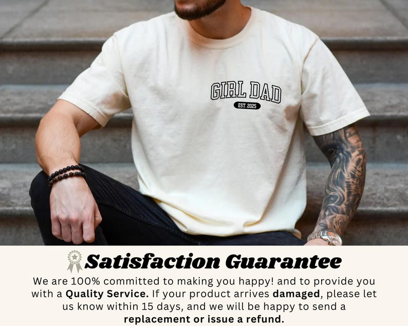 May include: Cream-colored t-shirt with the text "GIRL DAD EST. 2025" in black, featuring a classic collegiate font. The shirt is short-sleeved and has a relaxed fit. The image shows the shirt on a person sitting on steps.