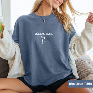 Puede incluir: Una camiseta azul vaquero con el texto "dance mom" y un lazo blanco.